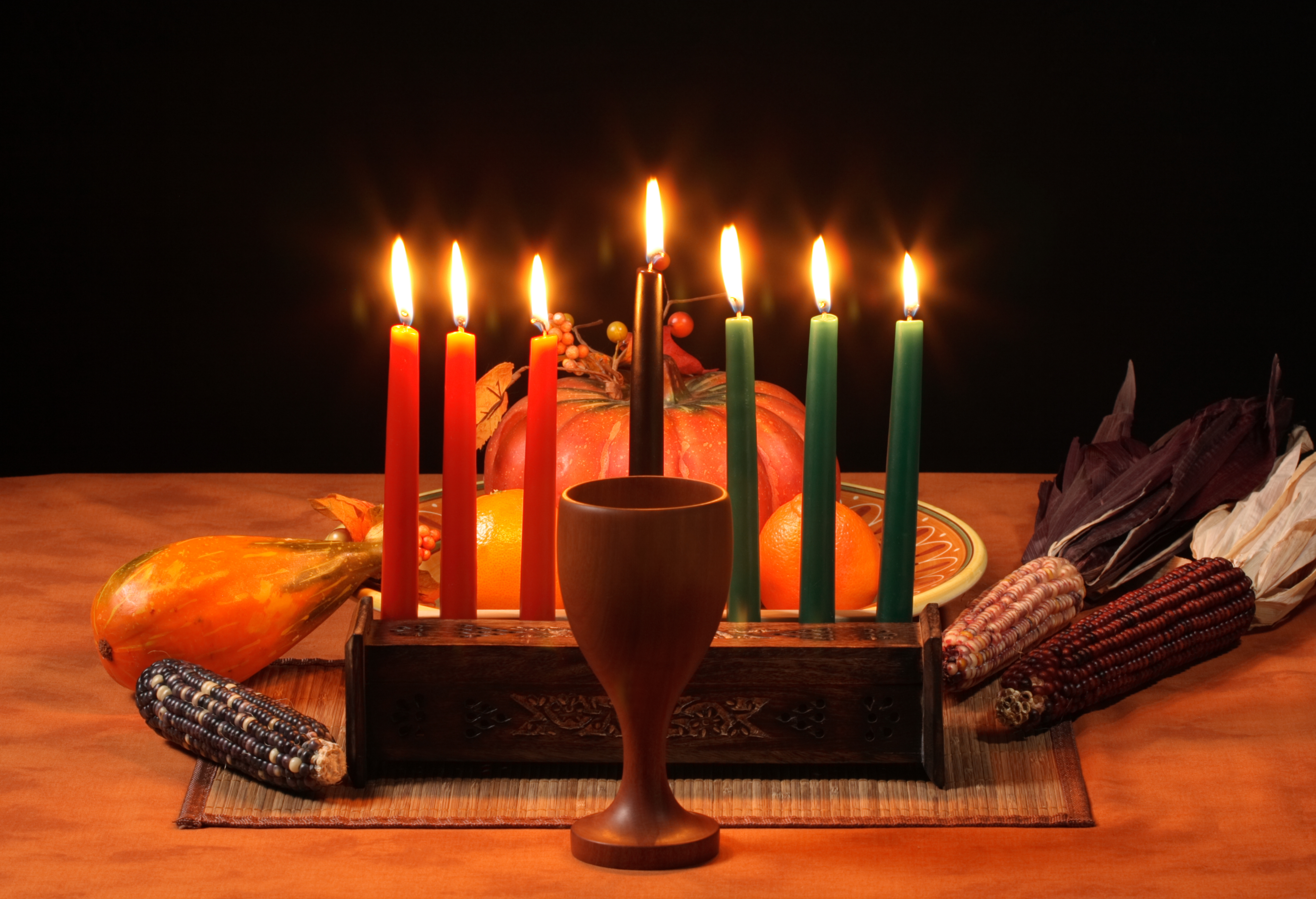 Burning candles with corn, a pumpkin and a goblet on a placemat.