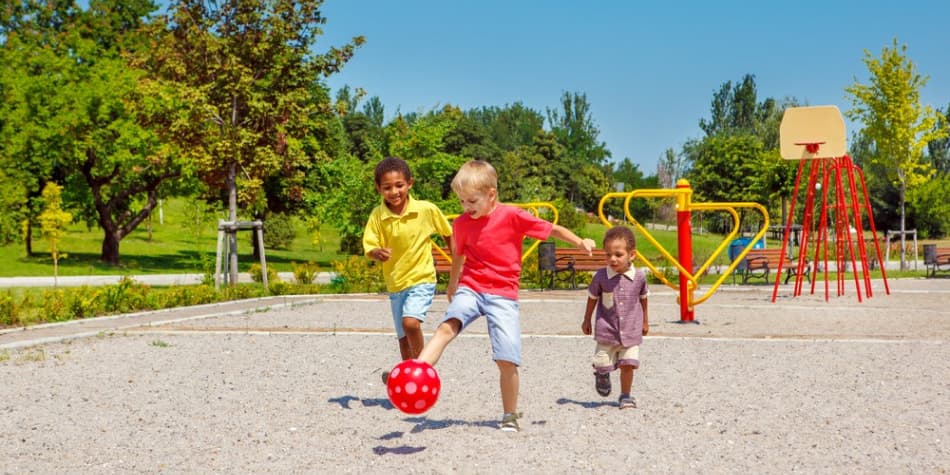 Three kids' kicking a ball in a playground.