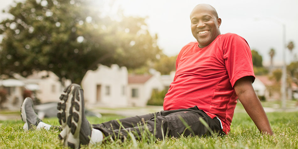 Man sitting in grass smiling, with athletic clothing on and his legs spread.