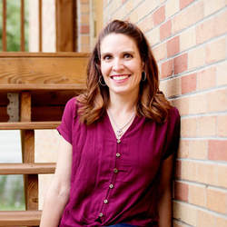 Doula Jessica Long wears a purple shirt and leans against a brick wall