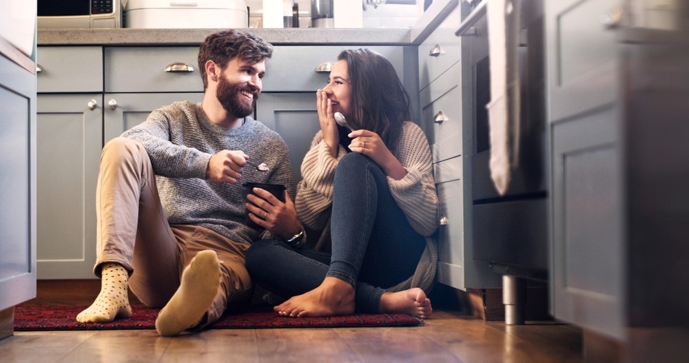 A couple shares a dessert on the kitchen floor.