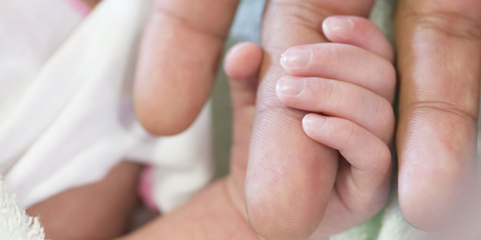 A newborn baby holds an adults finger in their hand.