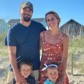 Kellen smiles while standing with his wife and his two kids on the beach.