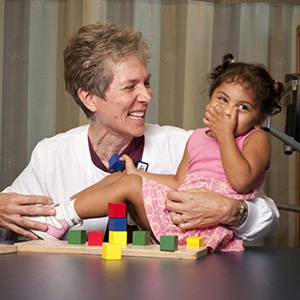 Occupational therapist holding a young child, both laughing.
