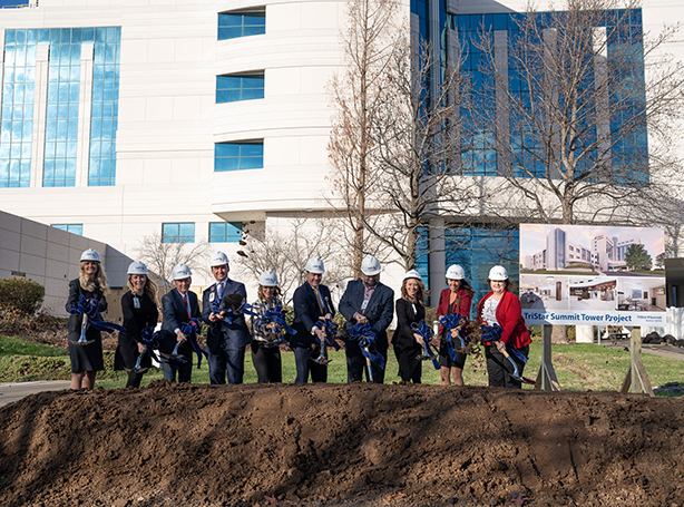 Hospital staff in business attire and helmets shovel dirt at groundbreaking ceremony.